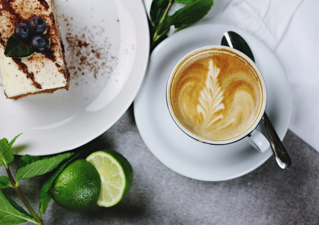 flat lay photography of coffee in teacup near plate of sliced cake